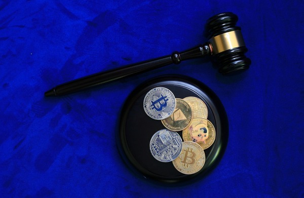 Judge gavel beside a tray of crypto coins on blue