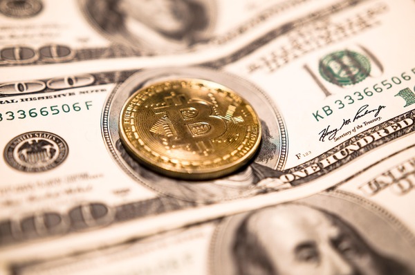 Gold crypto coin resting on hundred-dollar bills
